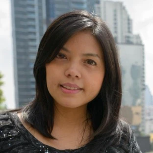 A smiling woman standing outdoors with a city skyline in the background, showing satisfaction after receiving a KuyaPlay free bonus.